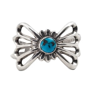 May include: A silver ring with a turquoise stone set in a sunburst design. The ring is shaped like a bow with intricate cutouts.