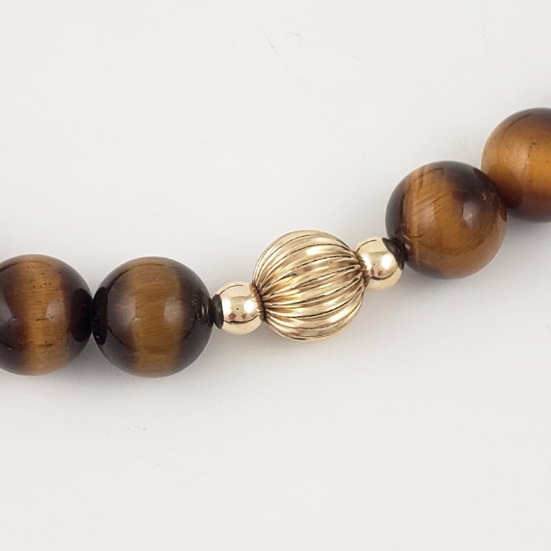 May include: A gold and brown beaded necklace with a large gold bead in the center. The beads are round and have a smooth, polished finish.