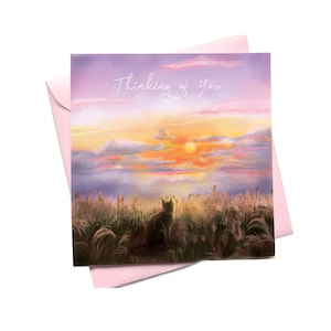 Può includere: Un biglietto d'auguri quadrato con una scena dipinta di un gatto seduto in un campo di erba alta al tramonto, con nuvole viola e arancioni nel cielo. Il testo "Thinking of You" è stampato in bianco in alto. È inclusa una busta rosa chiaro.
