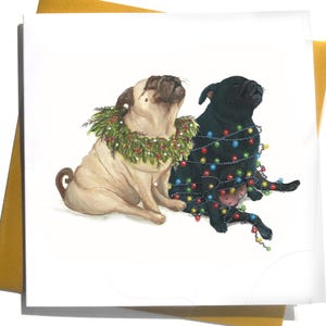 May include: A Christmas card showing two pugs. One is fawn-coloured and wearing a green wreath, the other is black and wrapped in colourful fairy lights. The card is on a white background with a gold envelope.