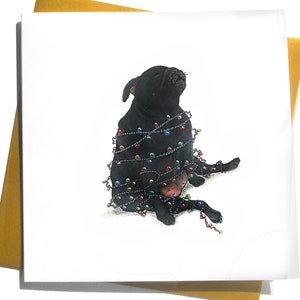 May include: A black dog, wrapped in a string of colorful Christmas lights, sits on a white background. The dog is looking up, with a slight smile. The image is a greeting card, with a gold envelope.