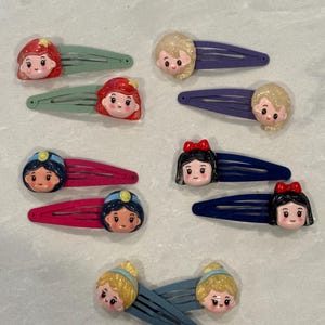 May include: Set of ten princess-themed hair clips. Each clip features a different princess character with a colorful design. The clips are made of plastic and have a spring-loaded mechanism.