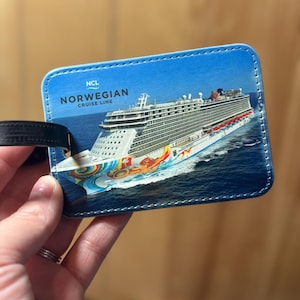 May include: A blue luggage tag with a white stitched border. The tag features a photo of a cruise ship with the text "NCL Norwegian Cruise Line" printed on it.