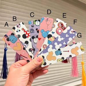 May include: A set of eight colorful bookmarks featuring a variety of Disney-themed designs, including Mickey Mouse ears, a waffle pattern, a backpack, a clock, a cupcake, a donut, a balloon, and a party hat. Each bookmark has a tassel.