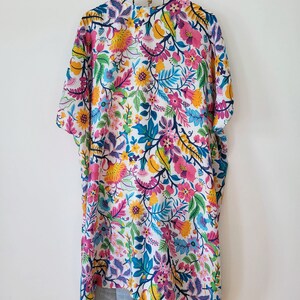May include: A white kimono with a colorful floral print. The kimono has a short sleeve and a tassel at the bottom.