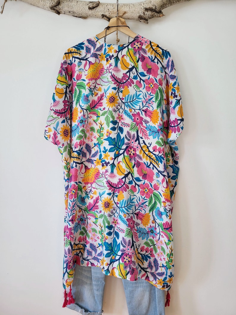 May include: A white kimono with a colorful floral print. The kimono has a short sleeve and a tassel at the bottom.