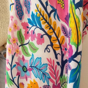 May include: A white fabric with a colorful floral pattern. The pattern features pink, blue, yellow, and green flowers and leaves.