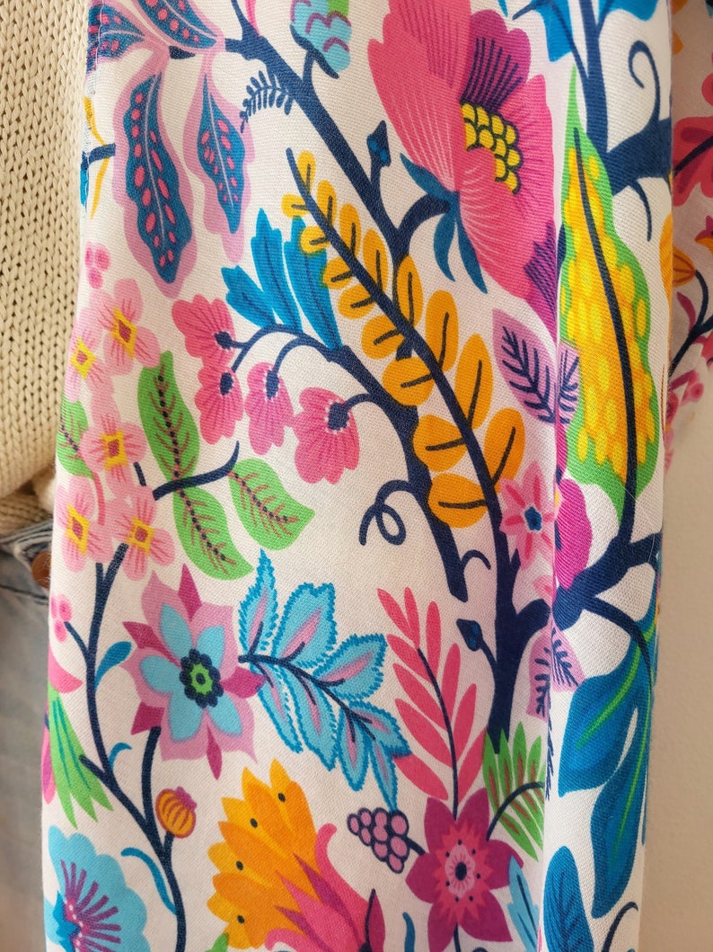 May include: A white fabric with a colorful floral pattern. The pattern features pink, blue, yellow, and green flowers and leaves.