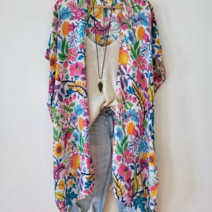 May include: A white kimono with a colorful floral print and pink tassels. The kimono is worn over a white tank top and blue jeans.
