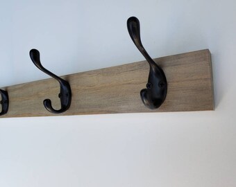 Könnte beinhalten: Ein Wand-Kleiderhaken aus Holz mit vier schwarzen Metallhaken. Der Haken ist aus hellbraunem Holz mit natürlicher Maserung.
