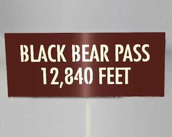 May include: A brown rectangular sign with white text that reads "Black Bear Pass 12,840 Feet".