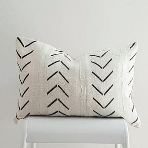May include: A white throw pillow with a black chevron pattern. The pillow is sitting on a white stool.