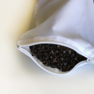 May include: A white pillowcase with a zipper open, revealing a filling of buckwheat hulls.