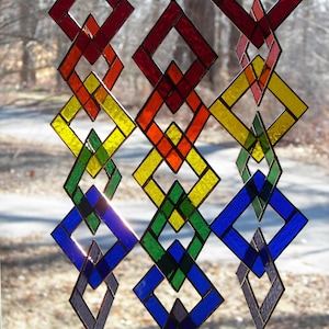 May include: A rainbow-colored stained glass mobile with diamond-shaped pieces. The mobile is made of glass and metal and is suspended from the ceiling.