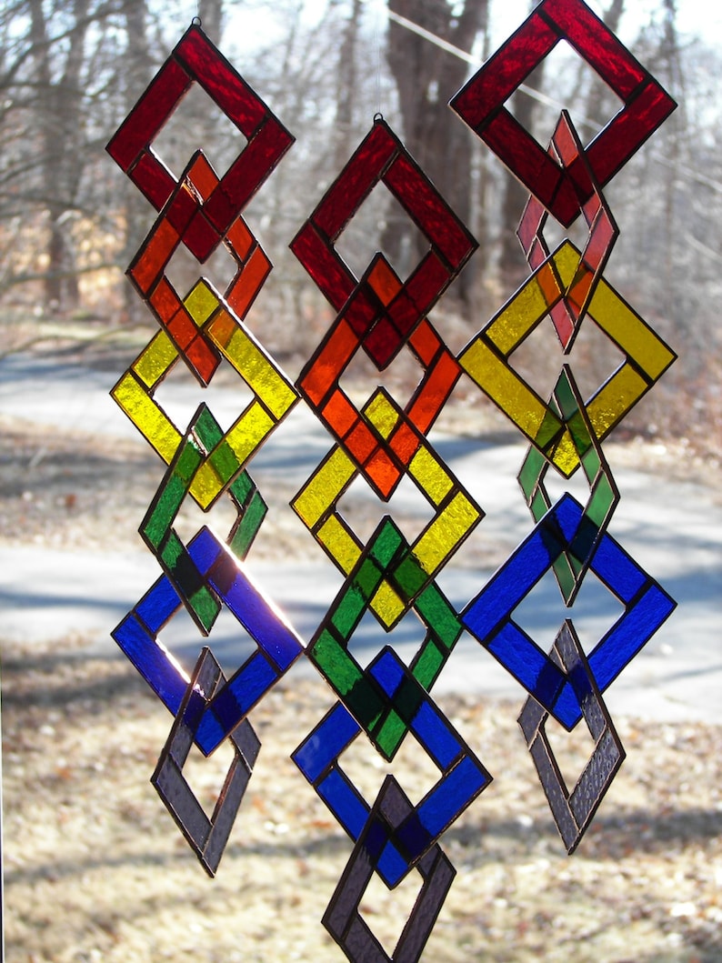 May include: A rainbow-colored stained glass mobile with diamond-shaped pieces. The mobile is made of glass and metal and is suspended from the ceiling.