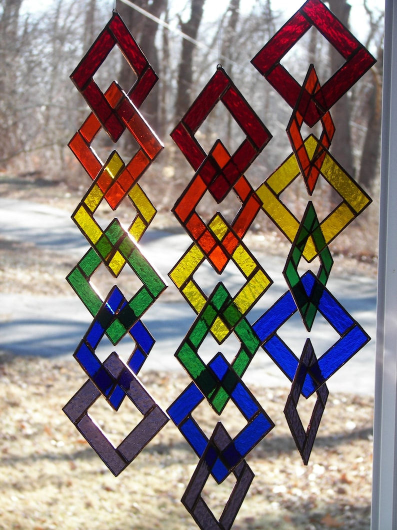 May include: A stained glass mobile with a rainbow of colors. The mobile is made up of interlocking diamond shapes. The colors are red, orange, yellow, green, blue, and purple.