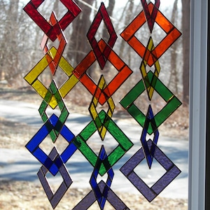 May include: A rainbow-colored stained glass mobile with diamond-shaped pieces. The mobile is made of glass and is hanging from a window.