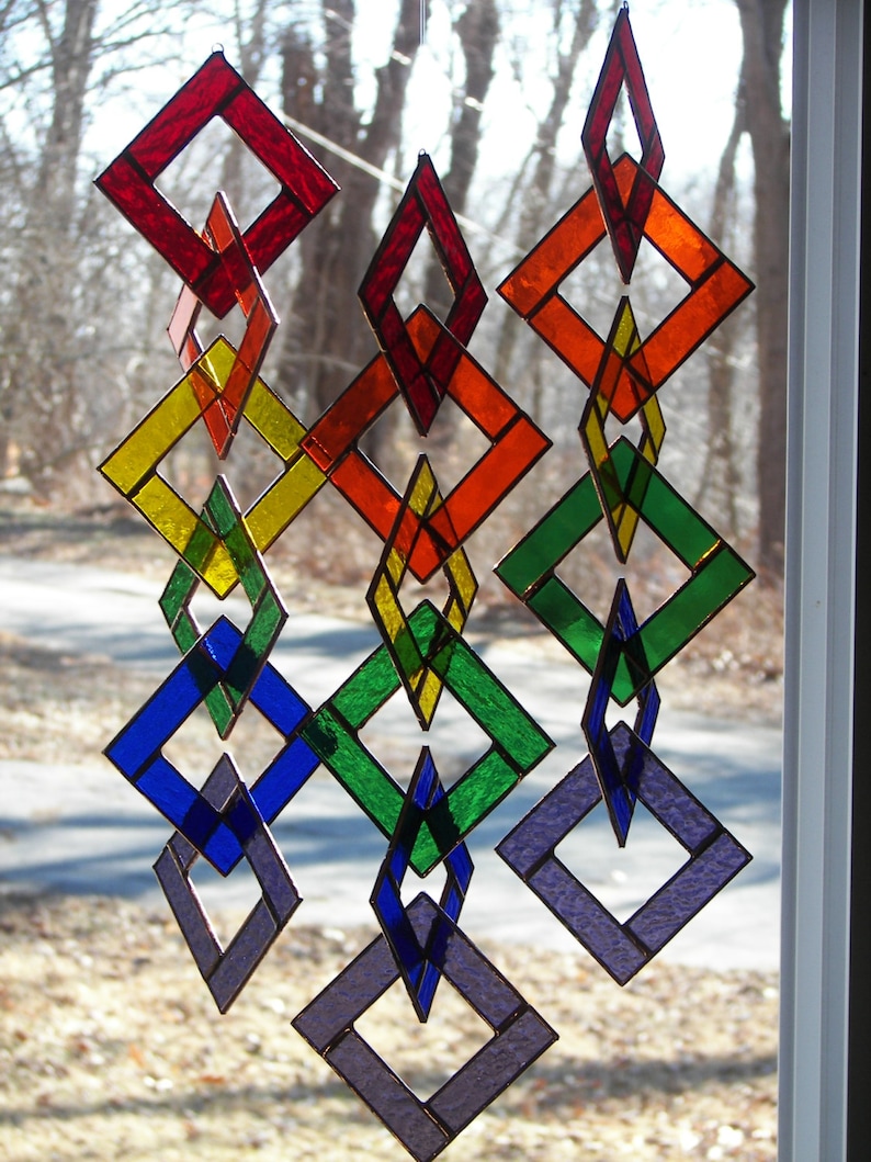 May include: A rainbow-colored stained glass mobile with diamond-shaped pieces. The mobile is made of glass and is hanging from a window.