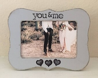 May include: A gray picture frame with a white mat and the words "You & Me" printed on the top. The frame has three small hearts at the bottom. The frame contains a photo of a couple in a desert setting.