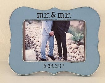May include: A light blue picture frame with a white border and a distressed finish. The frame has a photo of two people in it. The text "Mr. & Mr." is printed on the top of the frame and the date "6.24.2017" is printed on the bottom.