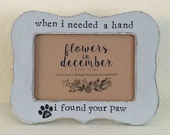 May include: A white picture frame with a paw print design and the text "when I needed a hand, I found your paw". The frame has a smaller picture inside with the text "flowers in December".