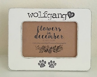 May include: White wooden picture frame with a black heart and the text "wolfgang" at the top. The frame has a smaller inner frame with a brown background and the text "flowers in december" and a website address. The frame has two black paw prints at the bottom.