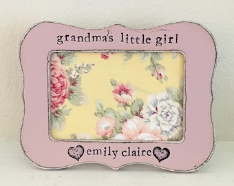 May include: A pink wooden picture frame with a floral pattern inside. The frame has the text "grandma's little girl" and "emily claire" on it.