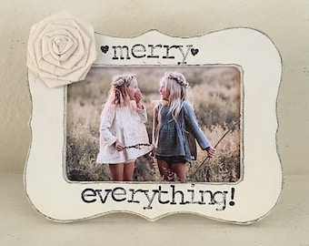 May include: White wooden picture frame with a white flower embellishment. The frame has the text "merry everything!" printed on it. The photo inside shows two girls smiling at each other.