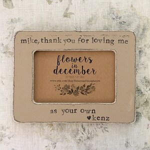 May include: A light brown wooden picture frame with a white border. The frame has the text "mike, thank you for loving me" at the top, "flowers in december" in the center, and "as your own ❤kenz" at the bottom.