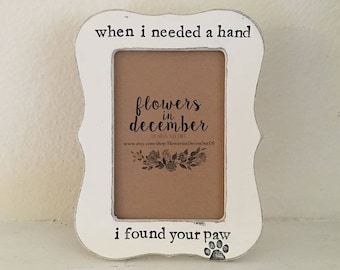 May include: White wooden picture frame with a paw print and the text "when I needed a hand I found your paw". The frame has a brown paper insert with the text "flowers in december" and a floral design.
