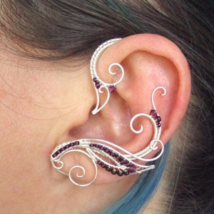 May include: Silver ear cuff with a delicate, intricate design featuring multiple swirls and small purple beads.