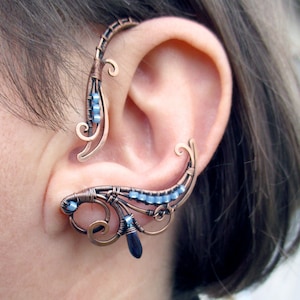 May include: A copper wire ear cuff with blue beads and a dangling blue gemstone. The cuff is designed to wrap around the upper ear.