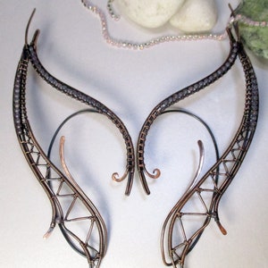 May include: A pair of delicate wire earrings shaped like wings, with a copper wire frame and gray beads along the edges.