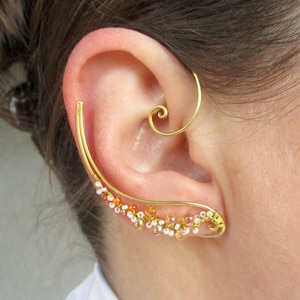 May include: Gold ear cuff with a spiral design and small white and orange beads.