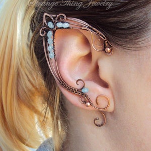 May include: Copper wire ear cuff with blue beads and a delicate design. The cuff is worn on the upper part of the ear and wraps around the ear.