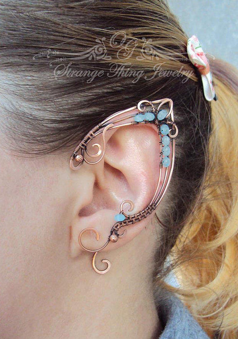 May include: Copper wire ear cuff with blue beads. The cuff is designed to wrap around the ear and has a delicate, intricate design.