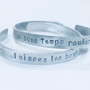 May include: Two silver bracelets with the French phrases "Laissez les bons temps rouler" and "Les bons temps rouler" engraved on them.