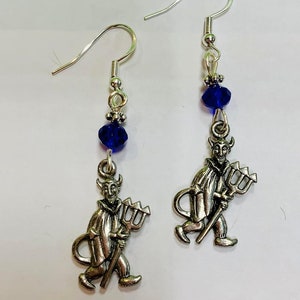 May include: A pair of silver earrings with blue crystal beads and a silver charm of a devil holding a trident.