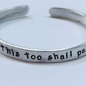 May include: Silver bangle bracelet with the inscription "This too shall pass".
