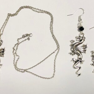 May include: A silver necklace and earrings set featuring a dragon pendant and black bead accents.