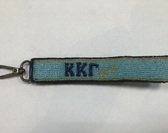 May include: A blue and gold beaded keychain with the letters "KKT" and a gold key symbol.