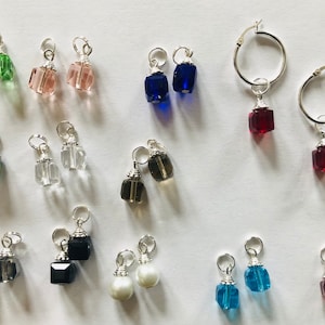 Puede incluir: Surtido de 18 pares de pendientes colgantes con diferentes encantos de cristal de colores. Los encantos son de forma cuadrada y están unidos a aros de plata.