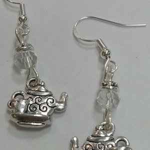 May include: Silver tone dangle earrings featuring a teapot and cup charm with a crystal bead accent.