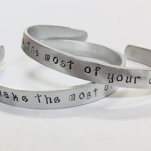 May include: Two silver bracelets with the inscription "Make the most of your dash" on one bracelet and "Make the most of" on the other bracelet.