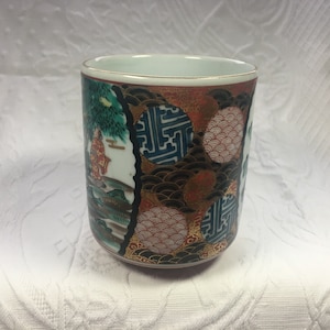 May include: A decorative ceramic cup with a gold rim, featuring a detailed Japanese landscape scene with figures and trees. The cup has a colorful design with red, blue, and gold accents, and a white interior.