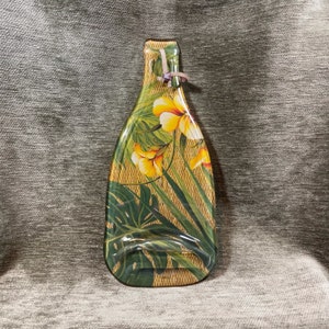 May include: Decorative bottle-shaped serving tray with a tropical floral design. The tray features a woven texture background with yellow flowers, green leaves, and a pink ribbon closure. The tray is approximately 15 inches tall.