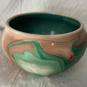 May include: A green and brown ceramic bowl with a marbled design. The bowl is handmade and has a unique, swirling pattern.