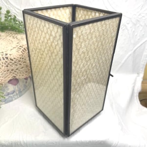 May include: A rectangular, stained glass lamp with a dark frame. The glass panels have a textured, off-white pattern. The lamp is a decorative item, likely for a living room or bedroom.