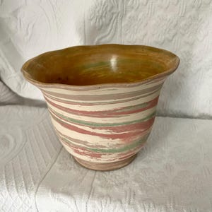May include: A ceramic planter with a scalloped rim and a marbled design in shades of pink, green, and beige.