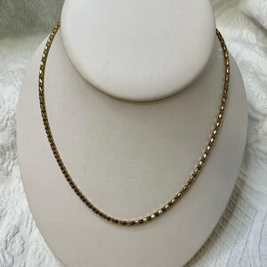 May include: A gold chain necklace with a braided design. The chain is on a white display stand.